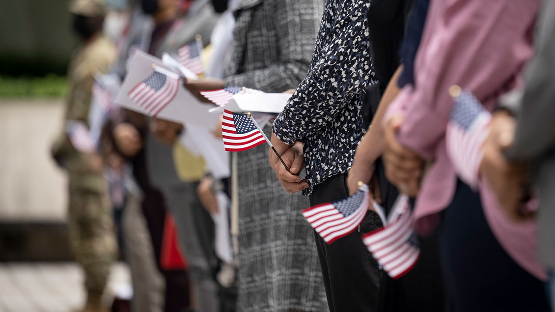 Individuals holding American flags at a public event, standing in a line.
